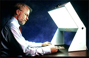 Image of man seated, reading a magazine while facing toward a light box for bright light therapy